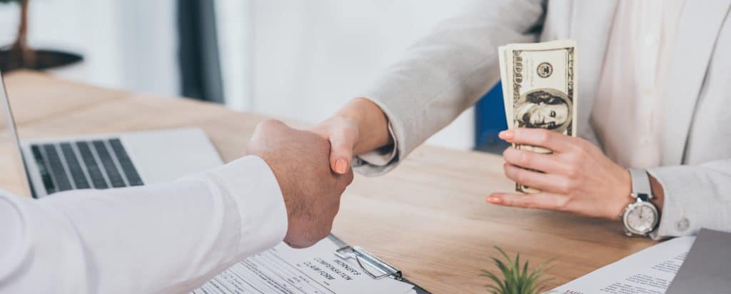 Vista recortada de una mujer de negocios dando la mano a un hombre y sosteniendo dinero en efectivo en el lugar de trabajo, concepto de compensación - Foto