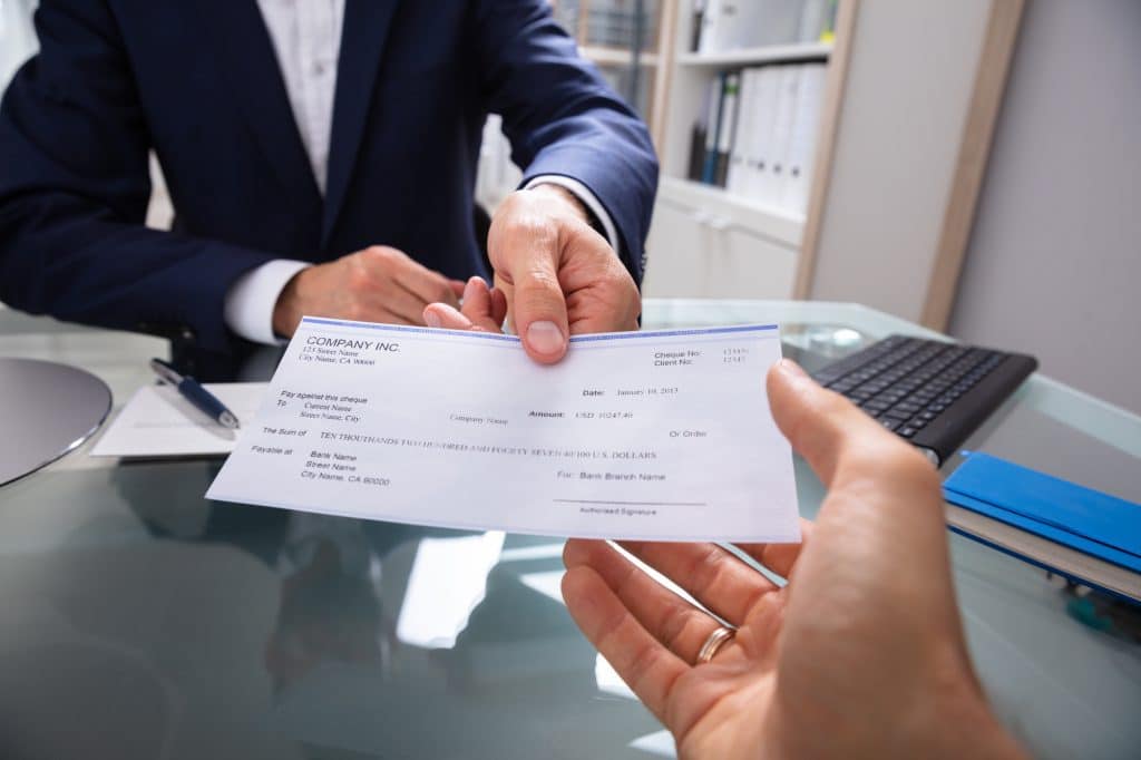 Businessman's Hand Giving Cheque Over Glass Desk