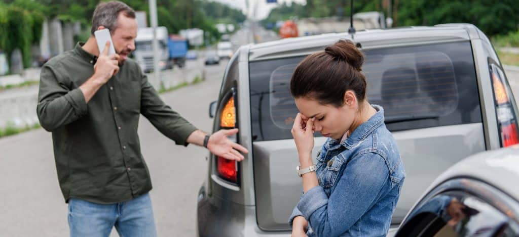 Un hombre y una mujer disgustados cerca de los coches tras un accidente de tráfico