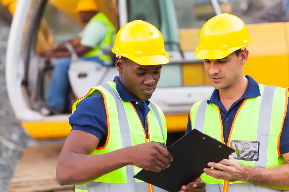 Construction co-workers discussing work plan at a construction site, wearing safety helmets and protective gear.