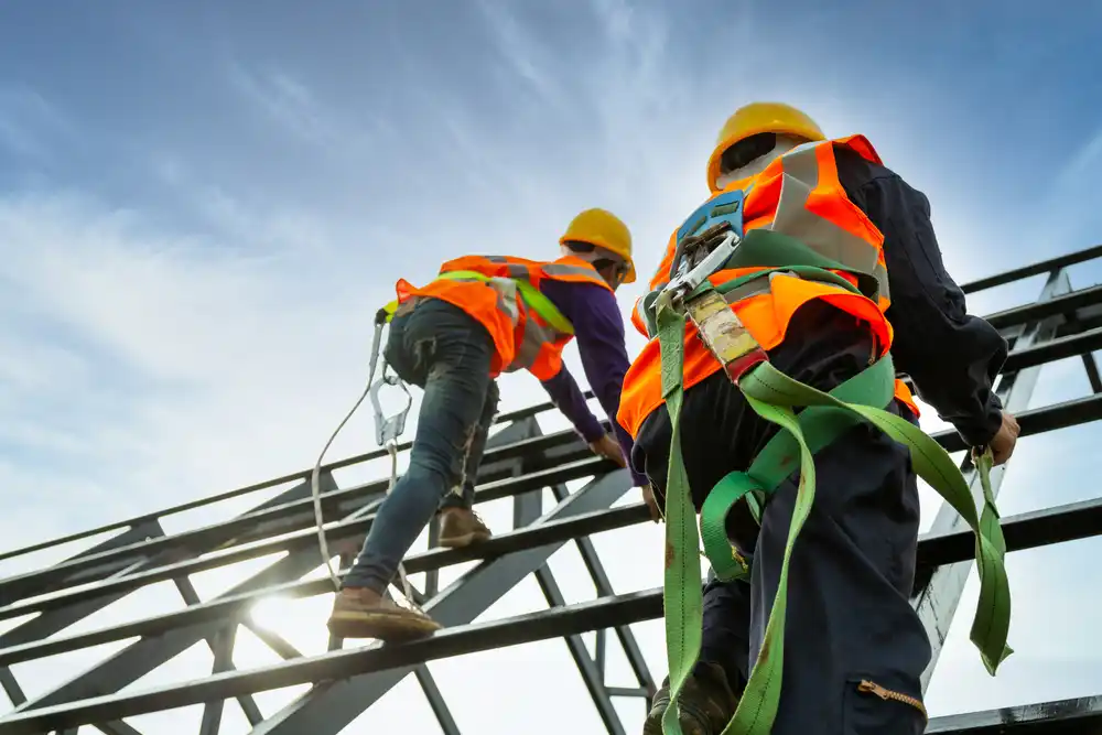 Construction worker wearing safety body harness with fall arrestor device while working at height on roof structure