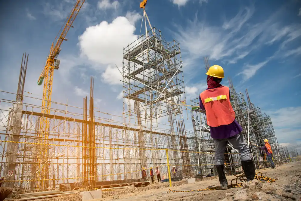 Construction workers installing scaffolding with crane at a construction site during sunset, emphasizing safety and teamwork.
